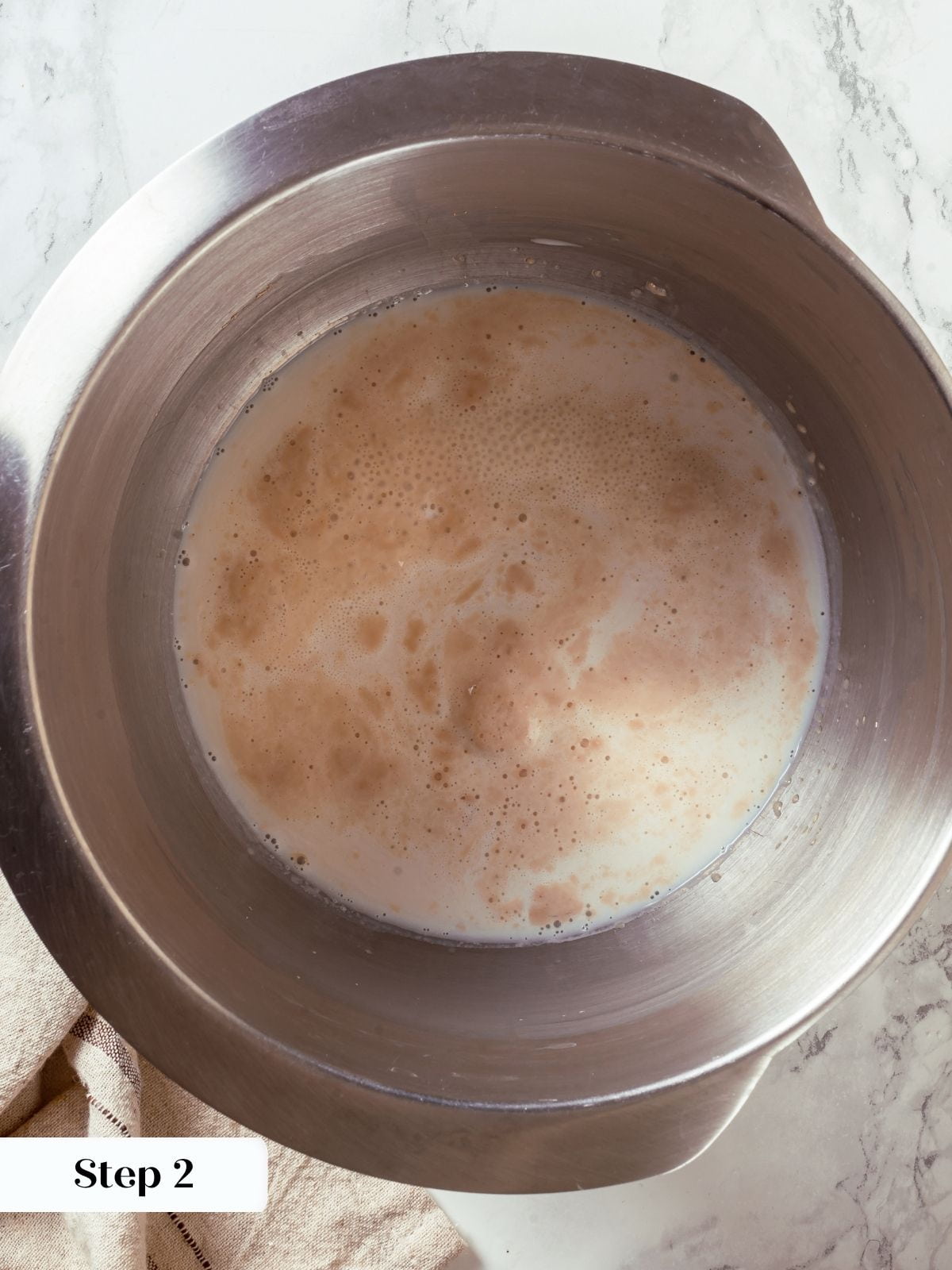Yeast bubbles in warm milk mixture, showing active fermentation stage before adding other ingredients.
