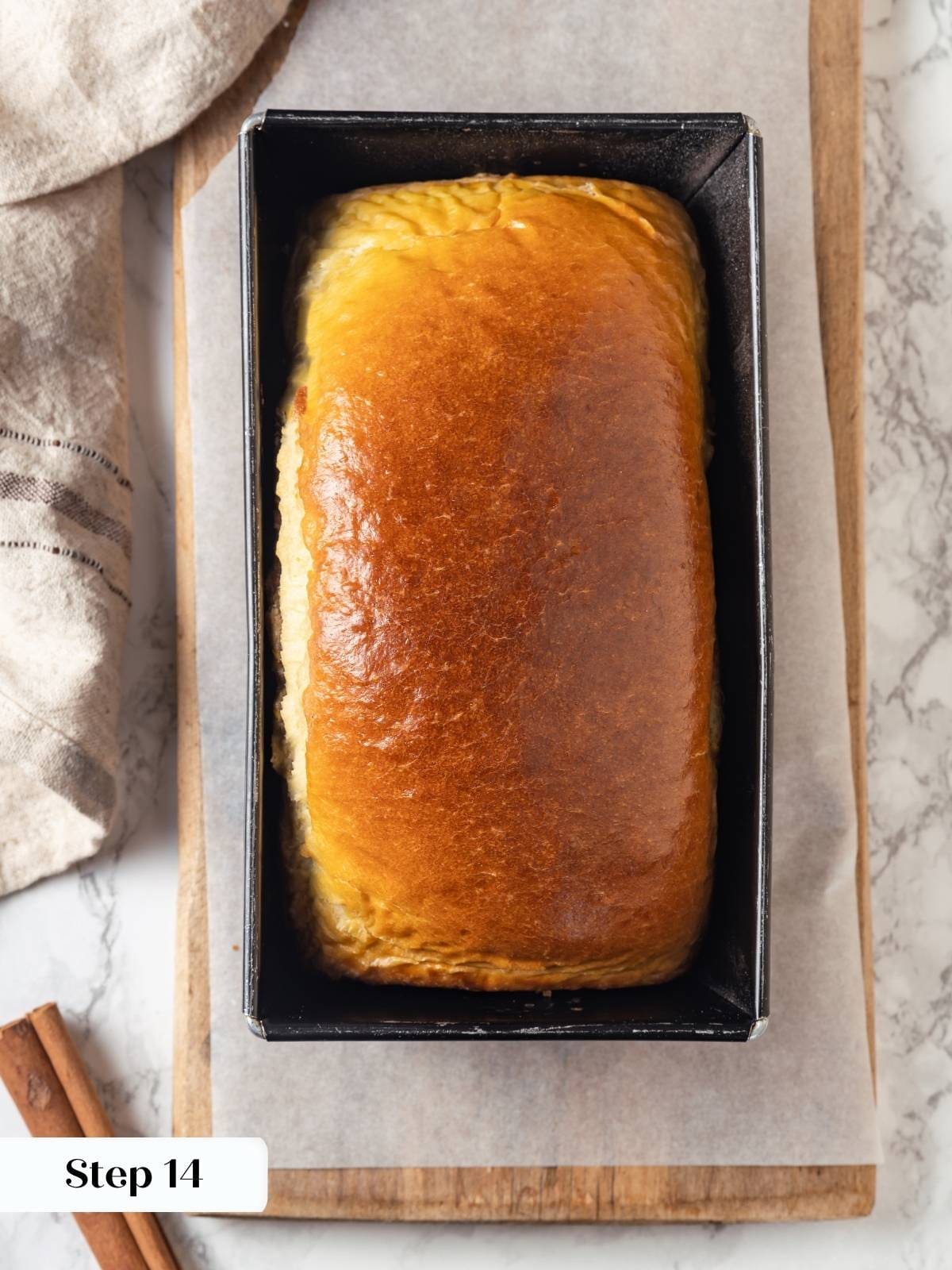 Loaf of cinnamon swirl bread rises tall in loaf pan after baking.