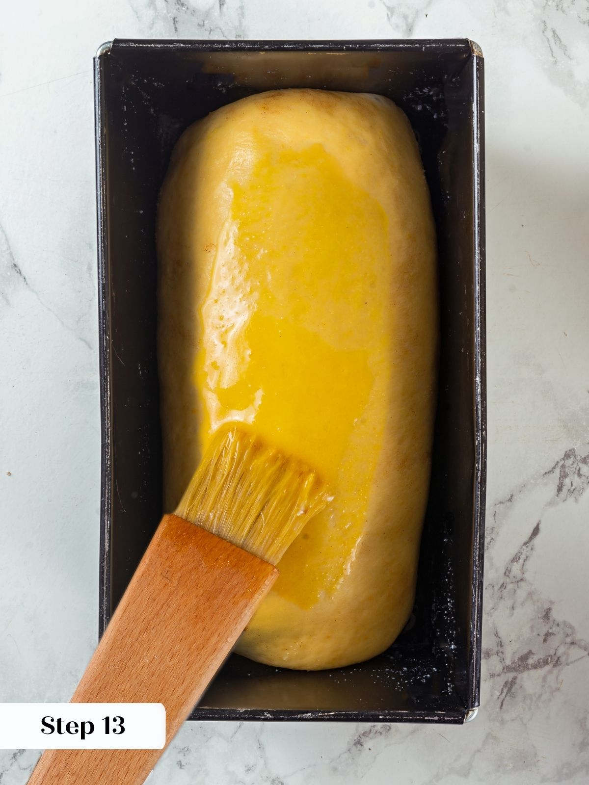 Dough log placed in a pan is brushed with egg wash to create shiny crust during baking.