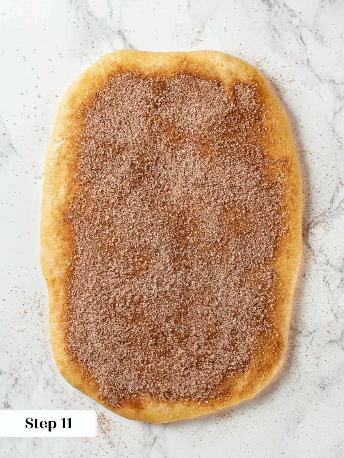 Rolled rectangle of dough is covered evenly with cinnamon sugar, ready to roll into log.