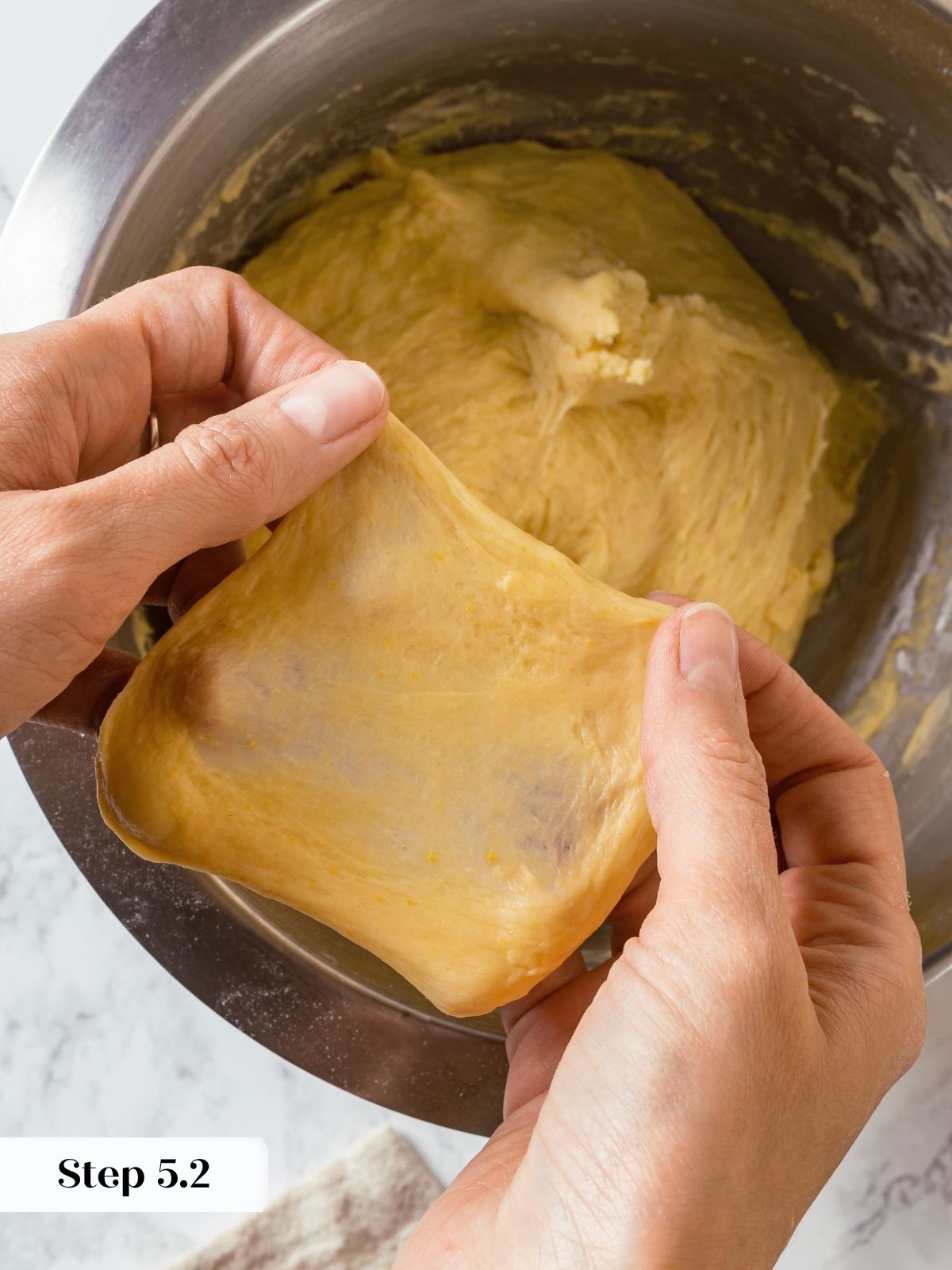 Dough is stretched thin between fingers to check gluten development with a clear windowpane test.