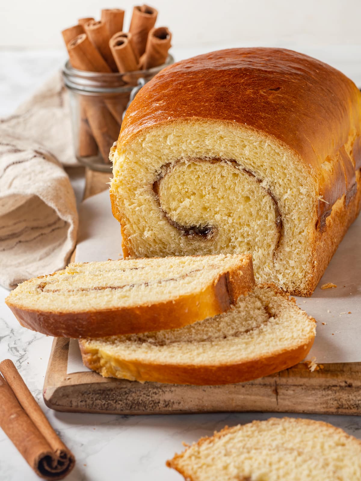 A loaf of cinnamon swirl bread is sliced to show soft interior and perfect swirl pattern.