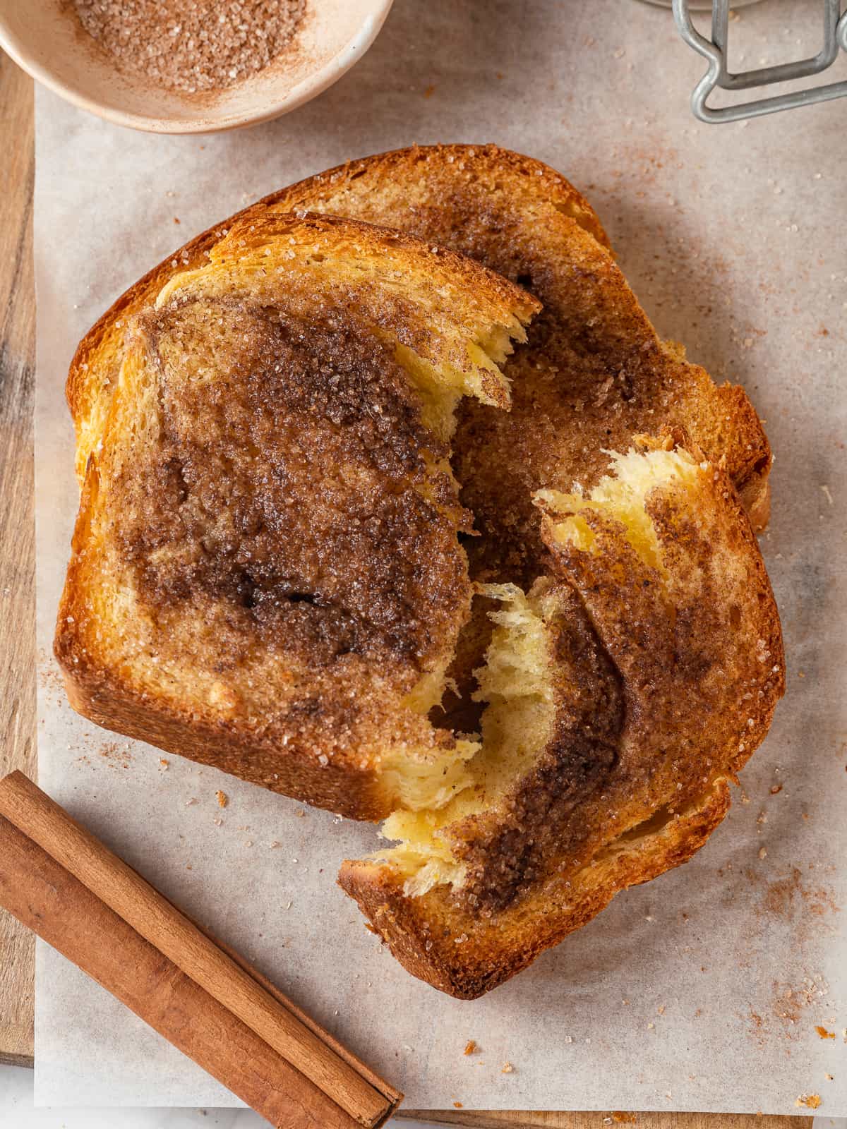 A broken piece of cinnamon toast reveals soft bread underneath a crisp caramelized cinnamon crust.