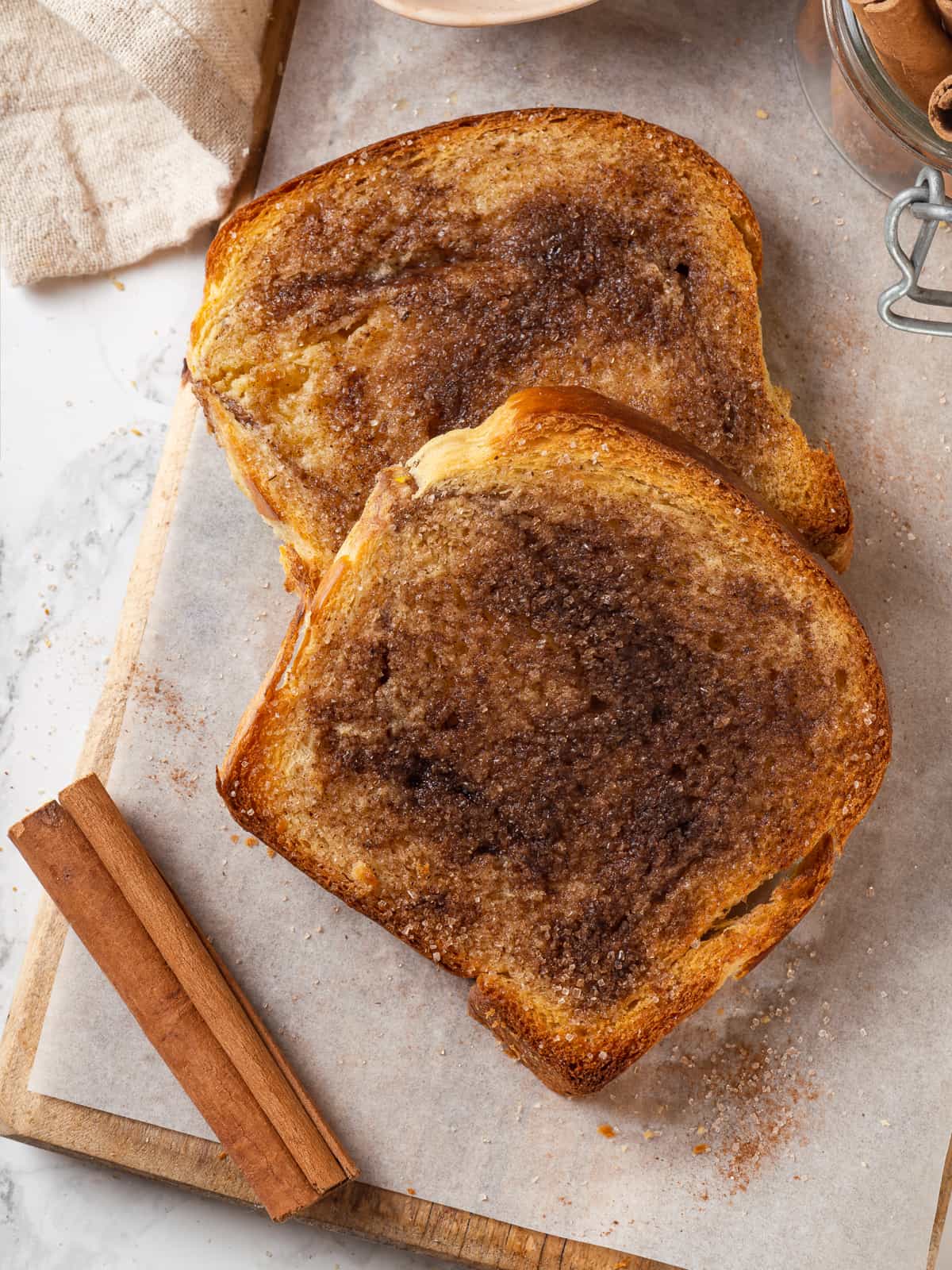 A cinnamon stick rests beside slices of prepared cinnamon toast for the toast topping.