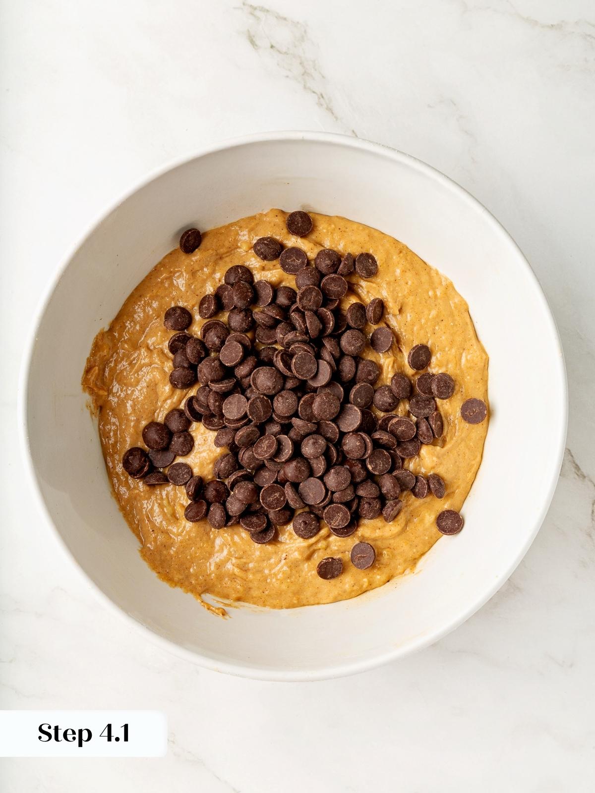 Chocolate chips resting on top of thick oat flour banana batter, ready to mix.