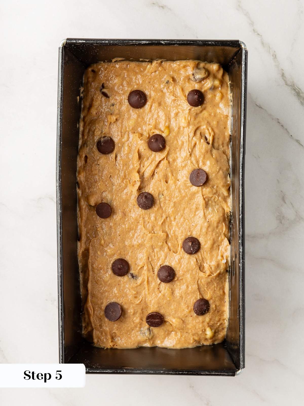 Prepared banana bread batter poured into loaf pan, smoothed and ready for baking.