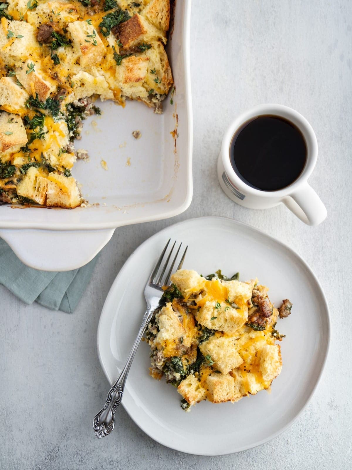 Slice of breakfast casserole beside a cup of coffee on a clean, light-colored counter.