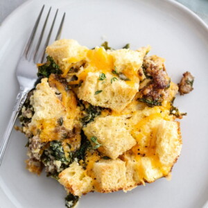 One portion on a dish, showing kale, sausage, eggs, and rustic bread inside.