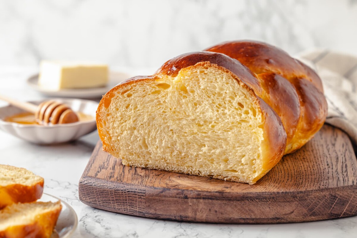 Finished challah loaf on a table with a wooden honey dipper and drizzled honey nearby.