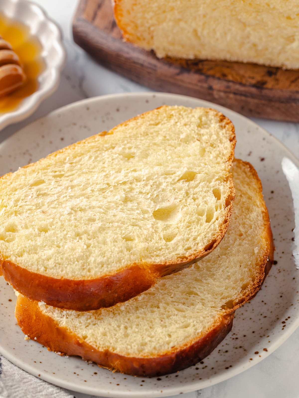 Thick slices of challah bread neatly plated for serving next to a butter dish.