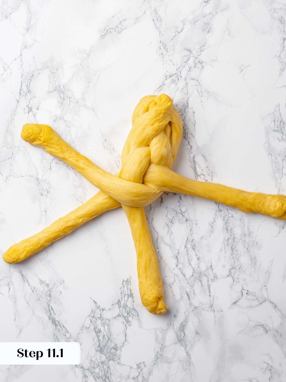 Mid-braid view of raw dough being woven into its final loaf shape.