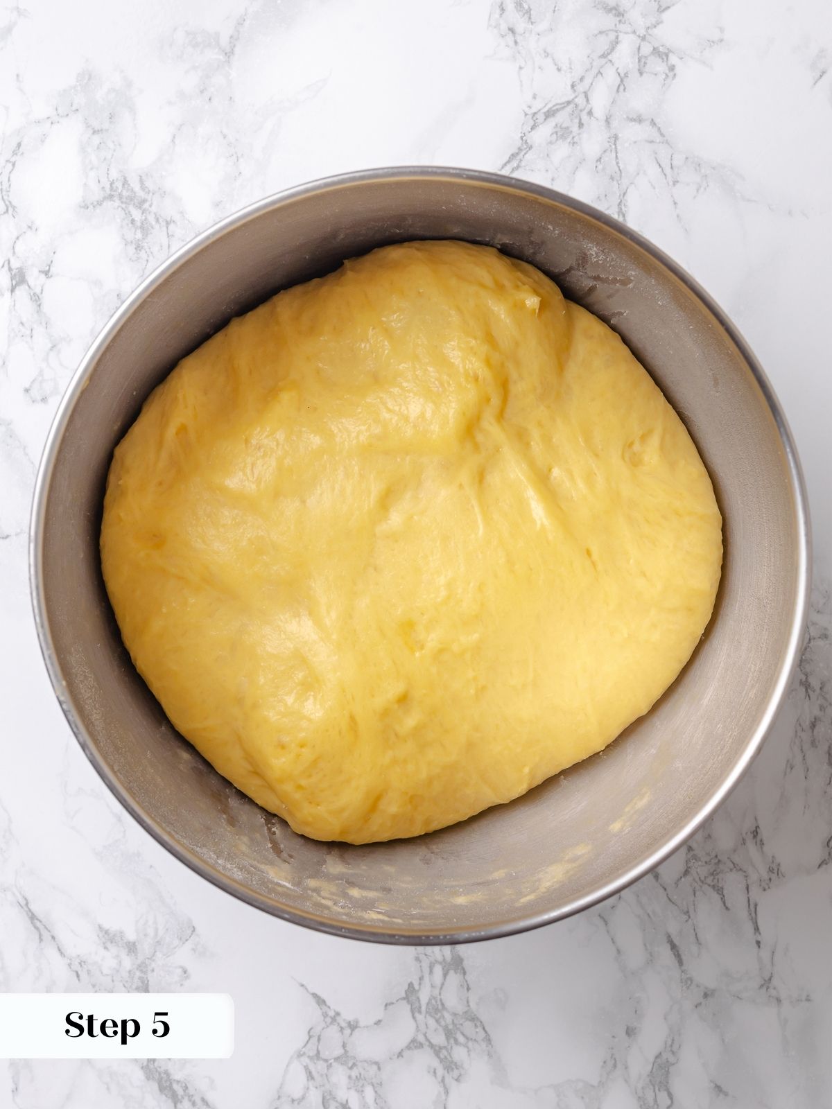 Dough in a bowl after bulk proofing, risen and smooth with a slight dome on top.