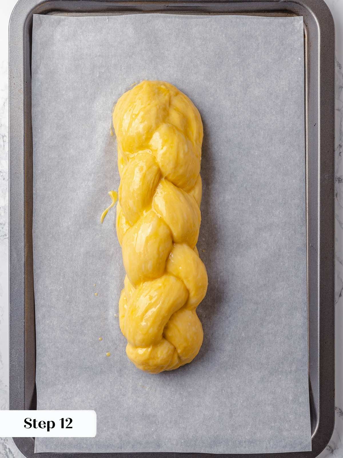 Unbaked challah dough resting on parchment-lined tray before entering the final proofing stage.