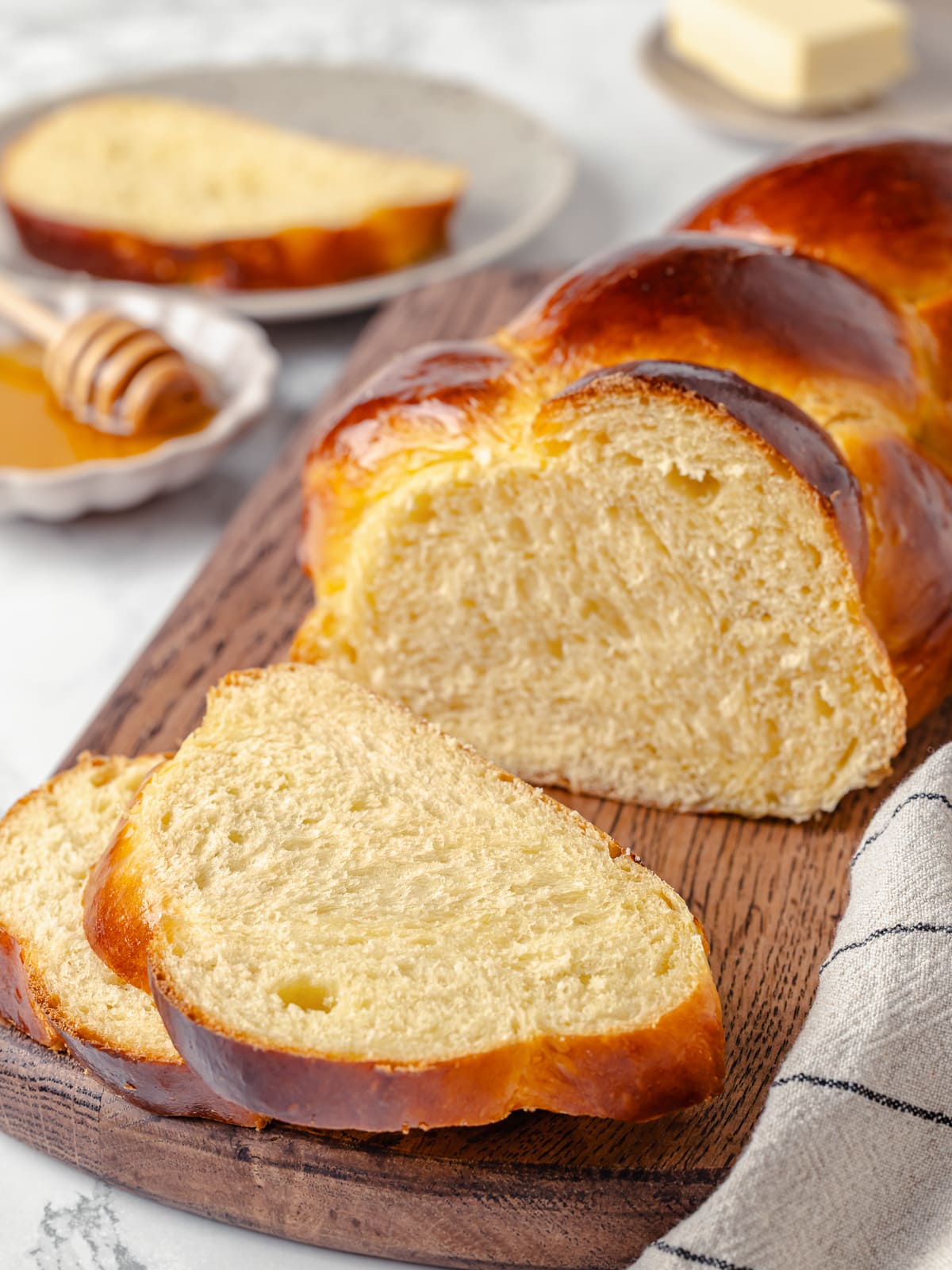 Challah loaf sliced into thick pieces, revealing glossy crust and soft crumb layers inside.