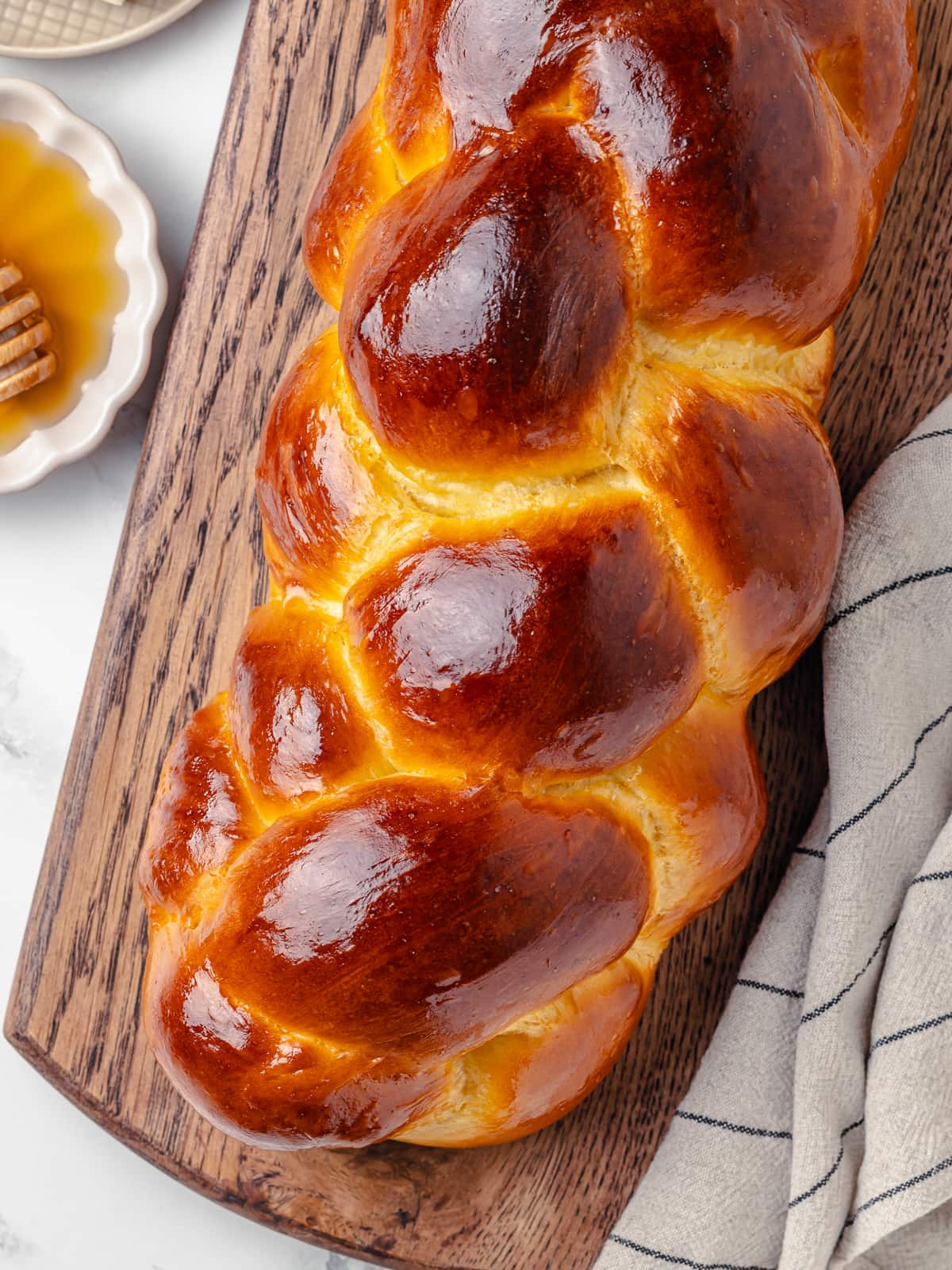 A freshly baked challah loaf on a wooden board with golden crust and twisted braid pattern.