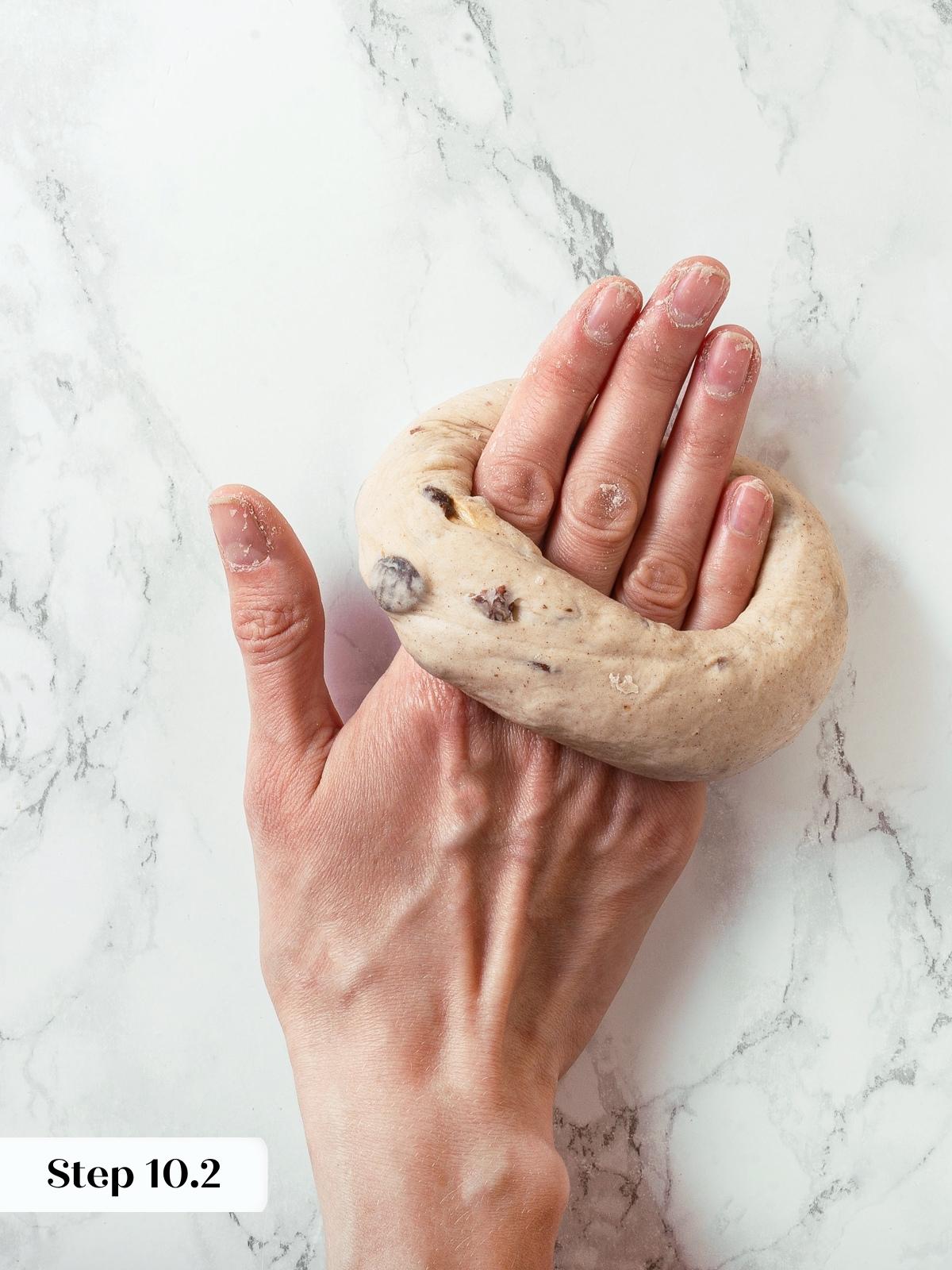 Hand flipping dough with palm to finish shaping the bagel.