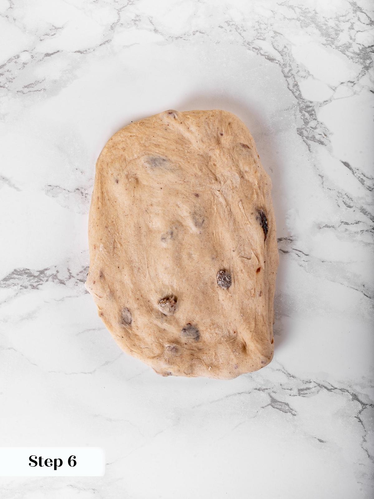 Dough rolled into a rectangle before folding, raisins just beneath the surface.