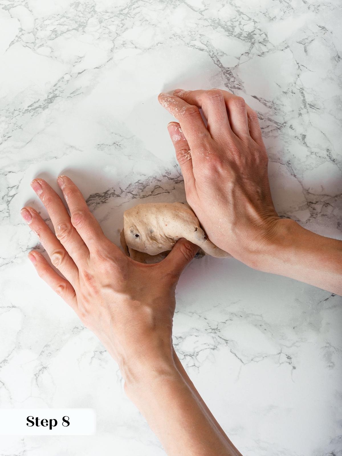 Dough log being shaped by hand with visible seams and light flour dust.