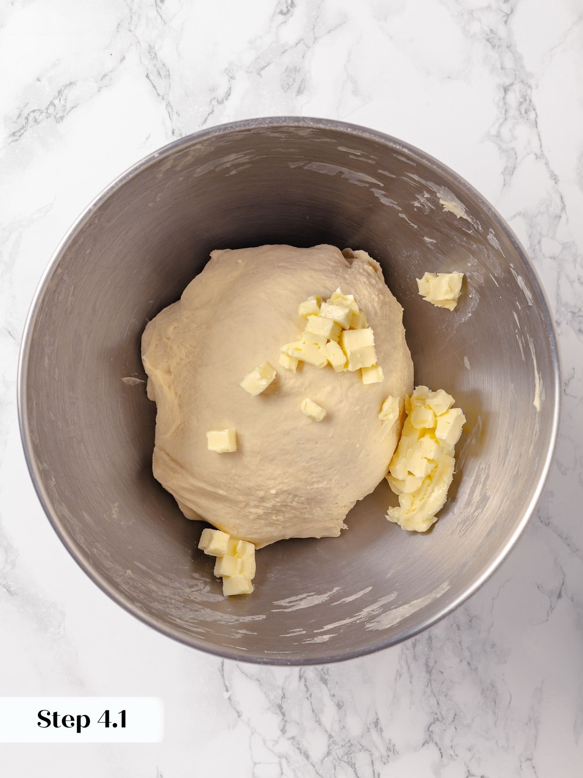Cubes of butter sitting on top of mixed dough, ready to be incorporated gradually.