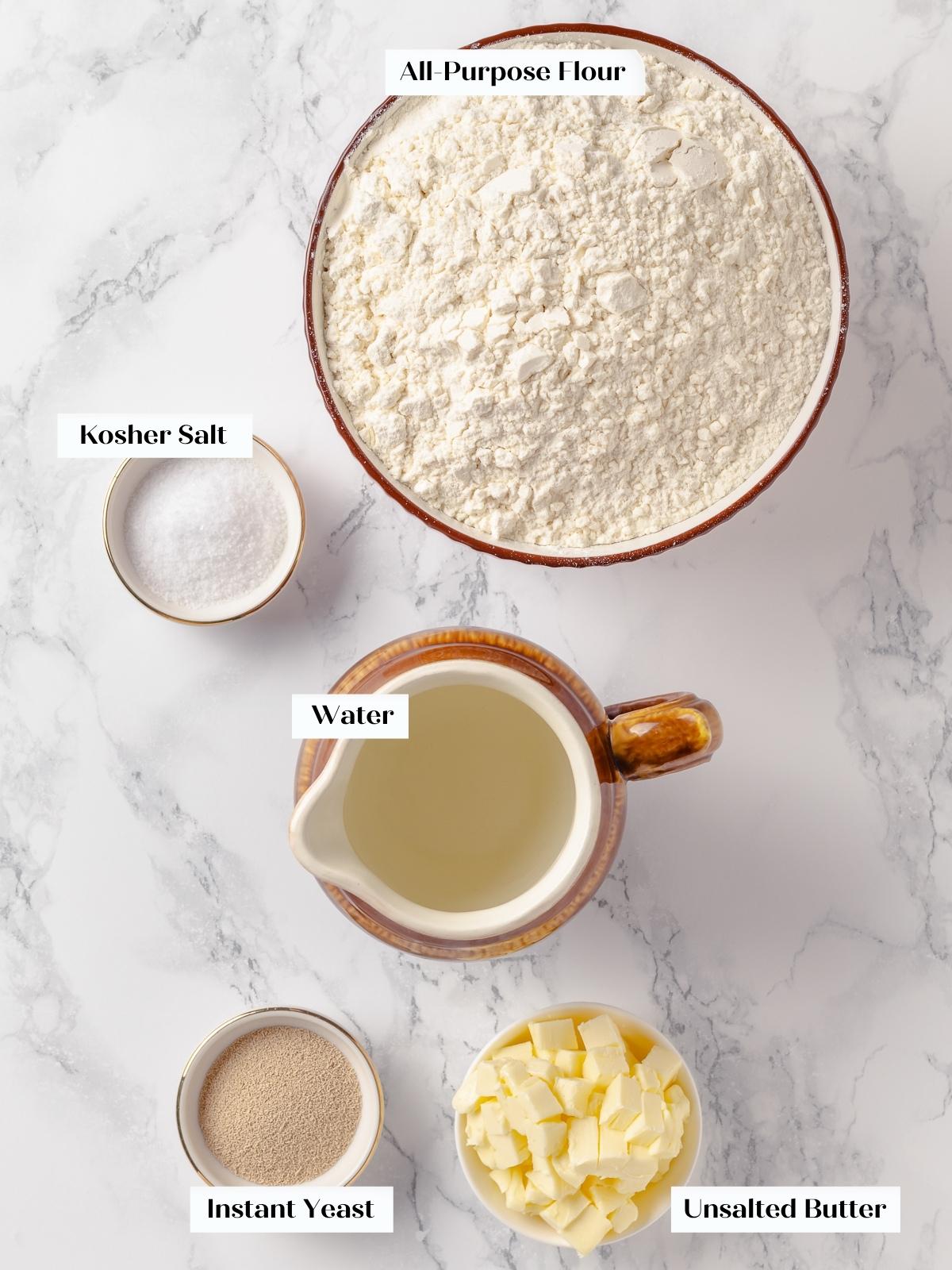 All ingredients for French bread measured and arranged clearly, including butter, flour, salt, and yeast.