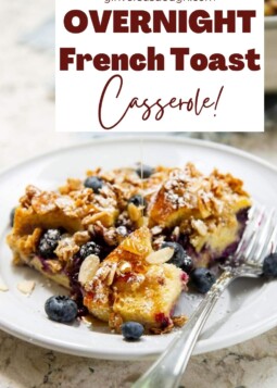 A slice of French toast casserole on a plate with extra berries and powdered sugar.