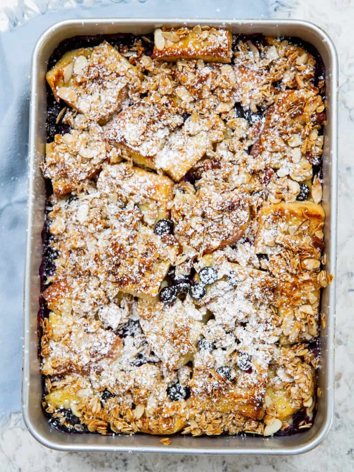 French toast casserole baked in a silver pan with visible blueberry bursts and browned topping.