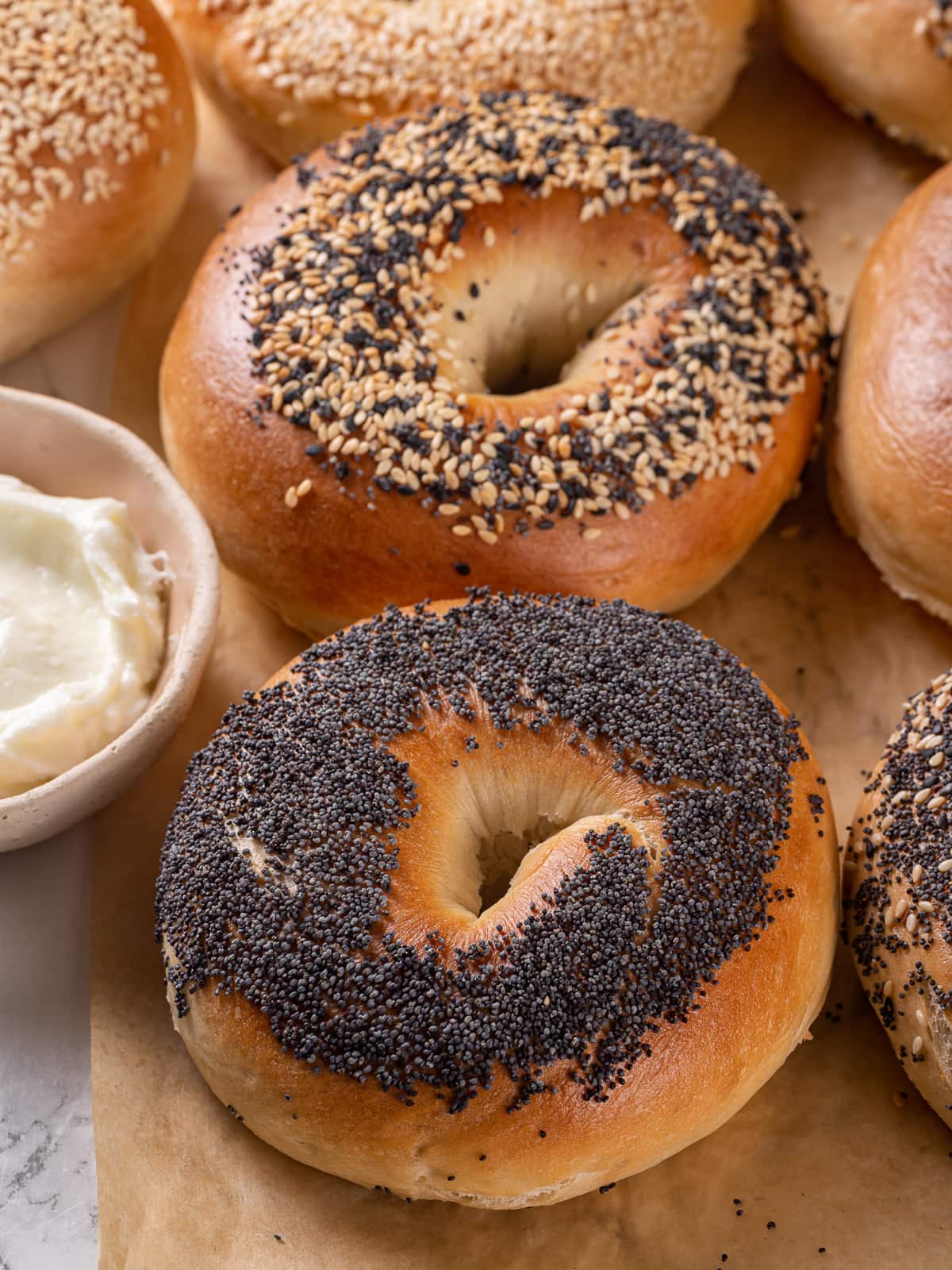 A freshly baked sourdough bagel generously coated in poppy seeds sits on parchment.