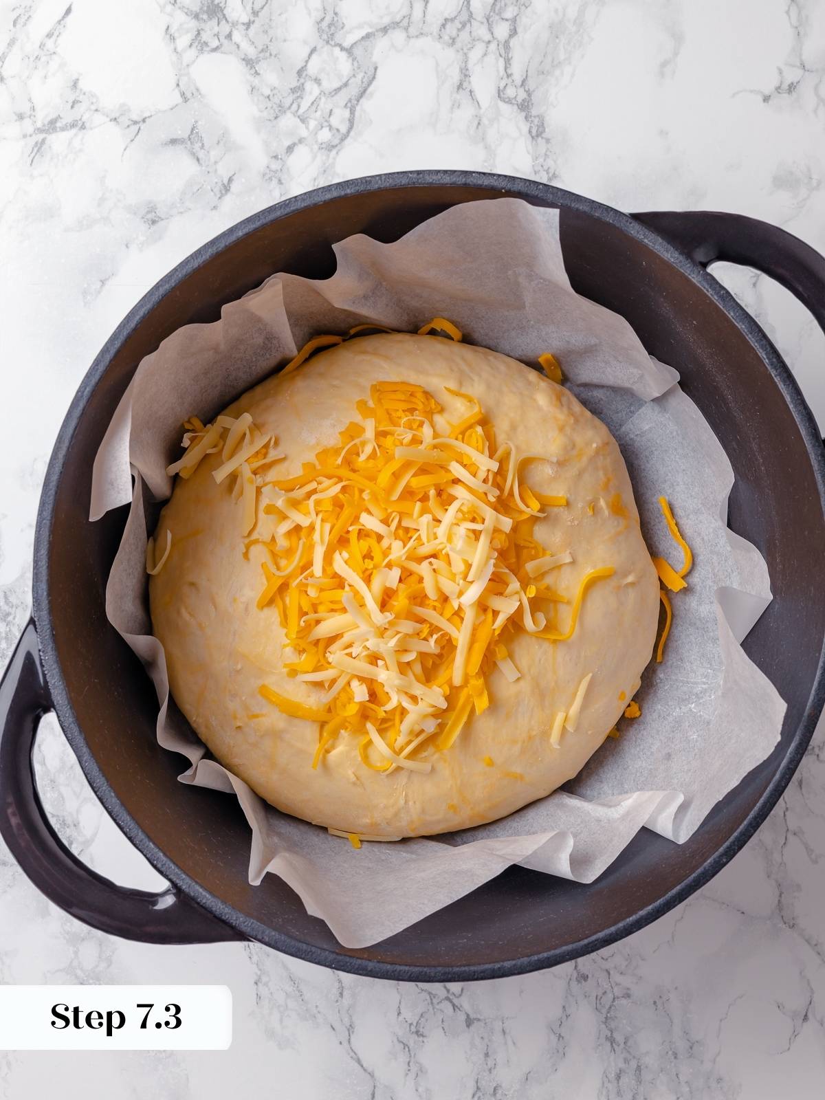 Cheese sprinkled on shaped dough before baking, inside a preheated Dutch oven.