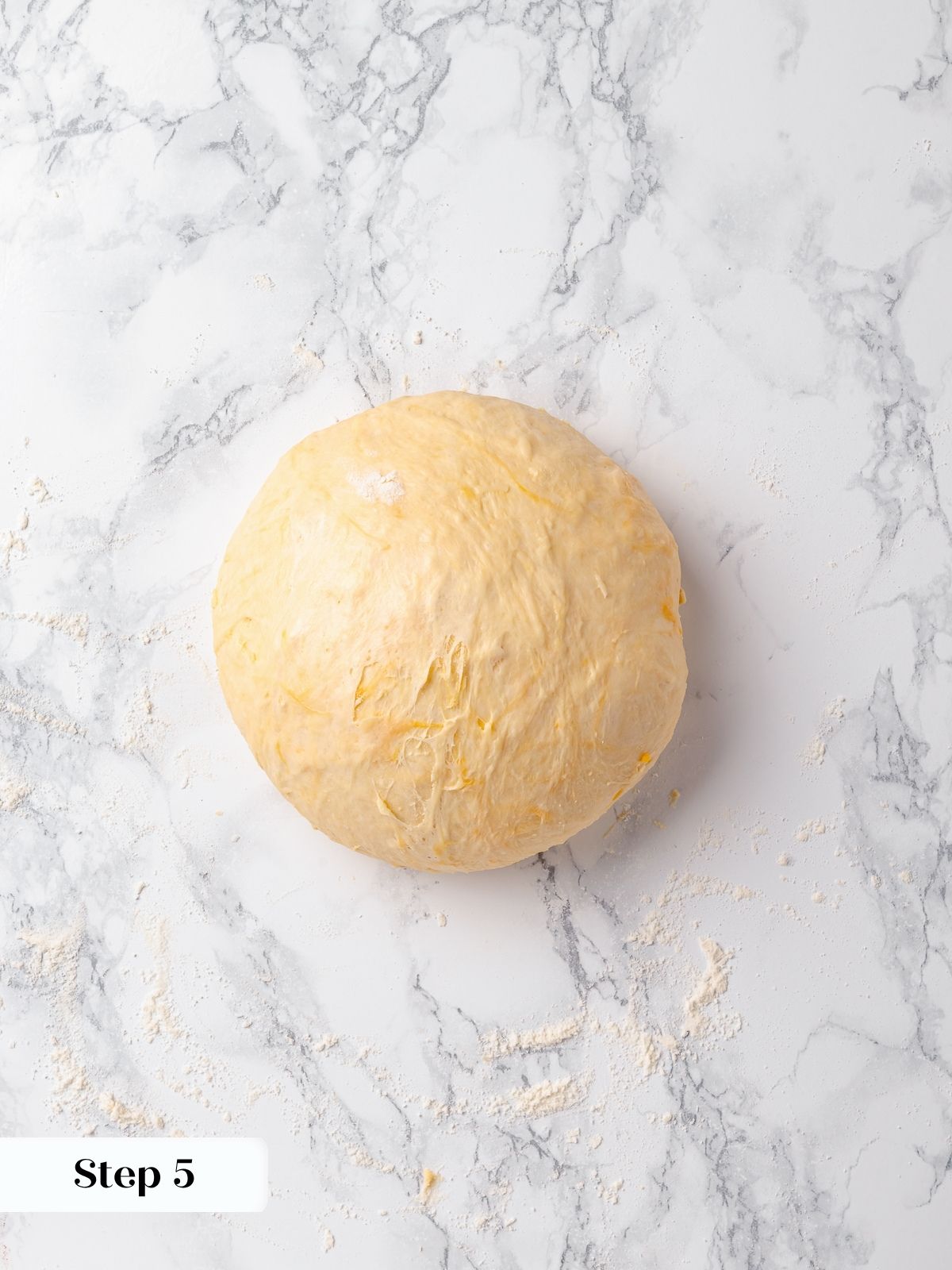 Dough shaped into a round ball on marble surface before final rise and scoring.