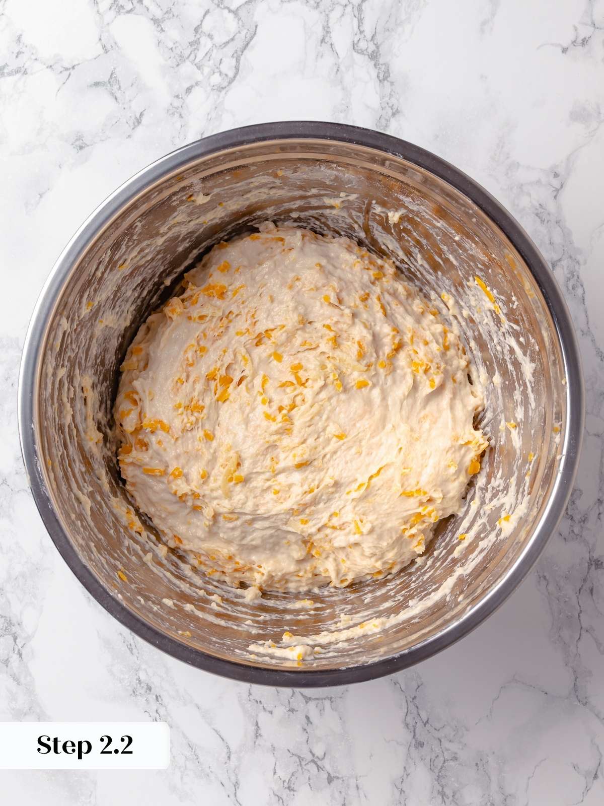 Shredded cheddar stirred into rough dough during early mixing of cheese bread.