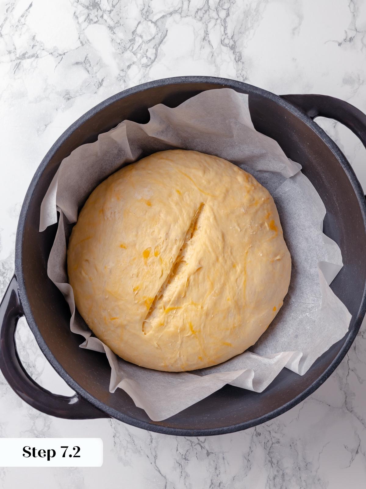 Dough resting in Dutch oven just before baking with cheese layered on top.