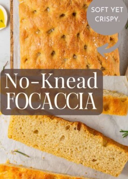 Crusty no-knead focaccia topped with herbs and sea salt resting beside a dish of olive oil.