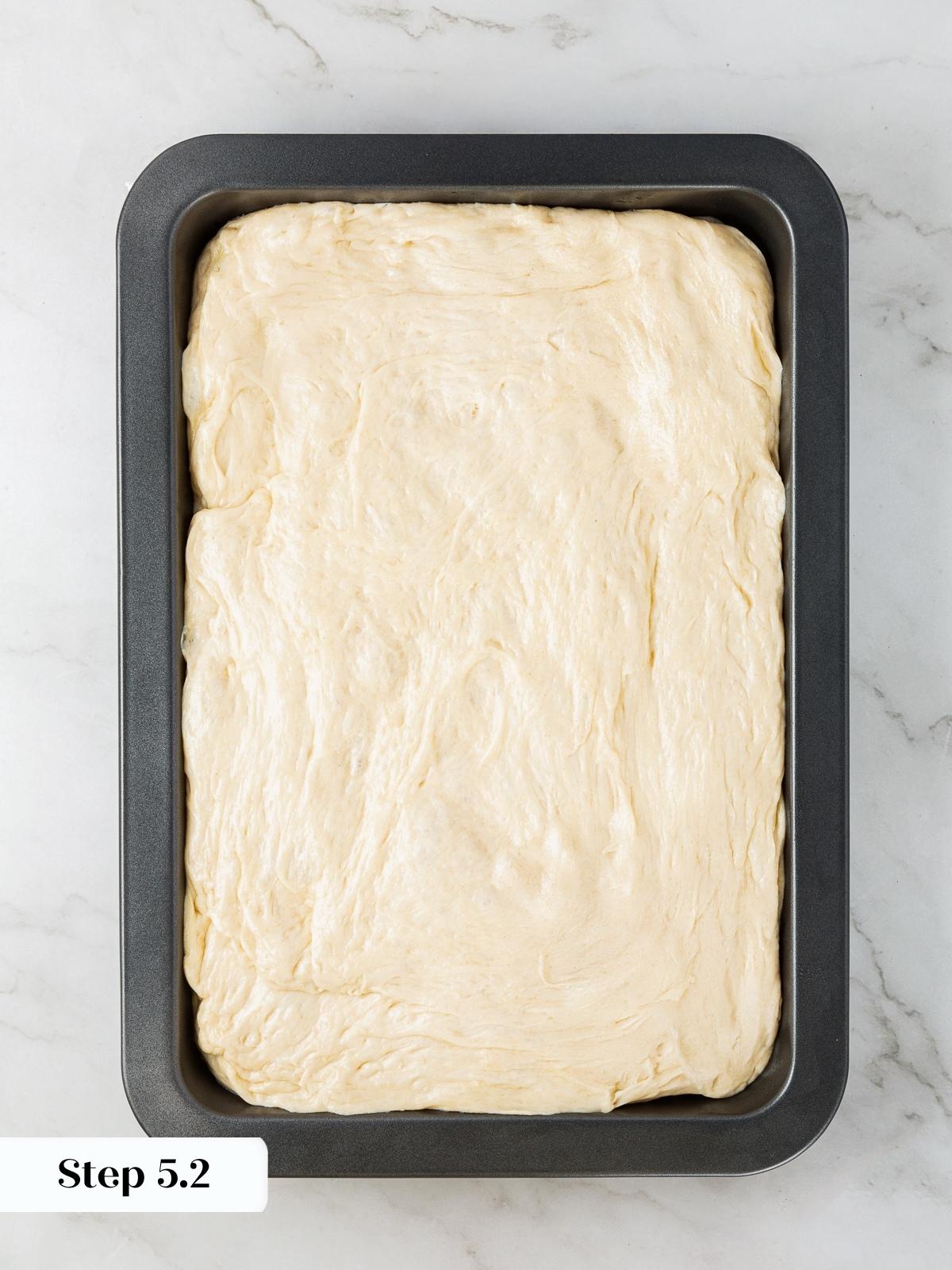 Stretched focaccia dough resting evenly in pan before final proofing step.
