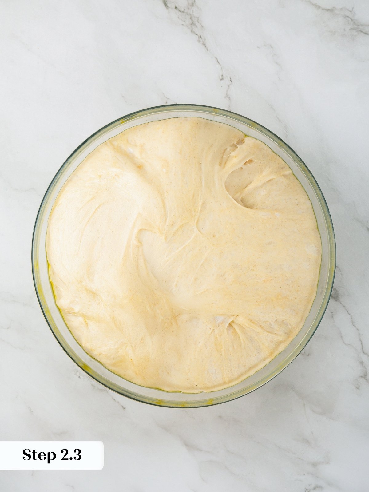 Focaccia dough doubled in size after initial rise in oiled glass bowl.