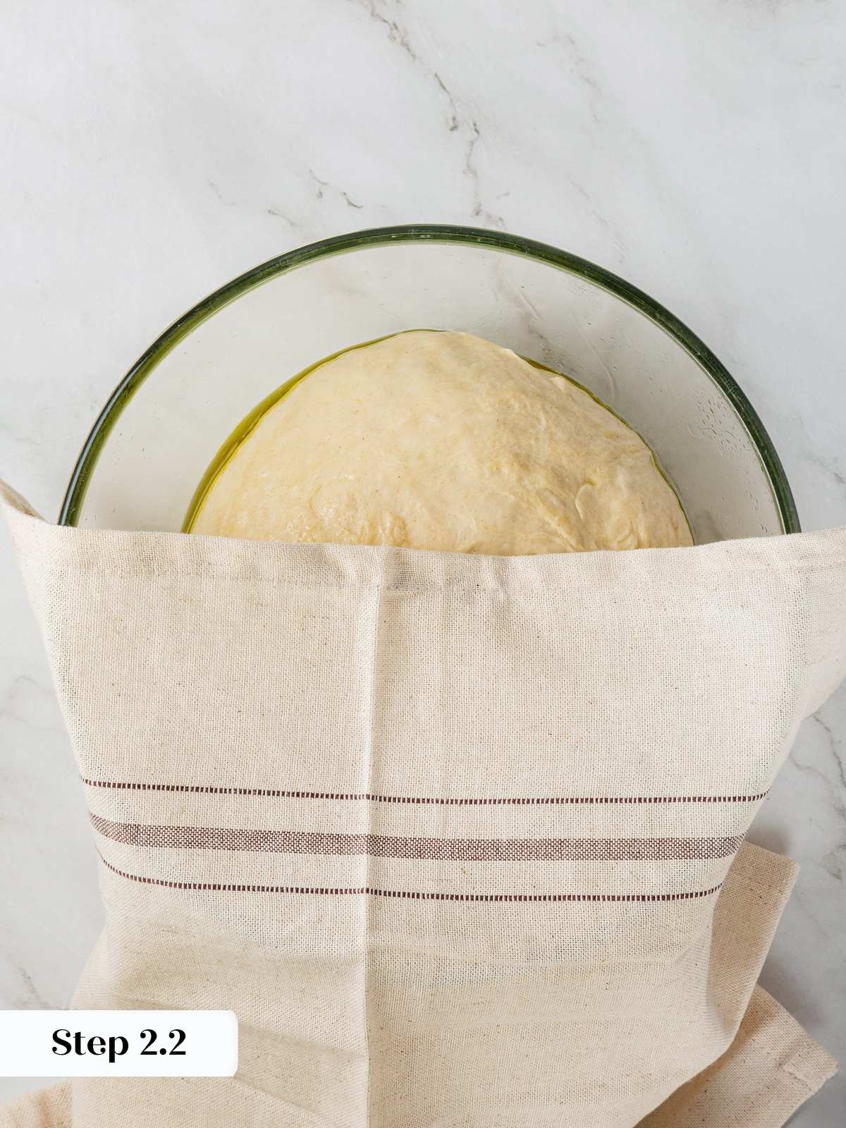 Soft kitchen towel draped over bowl of dough during early proofing.