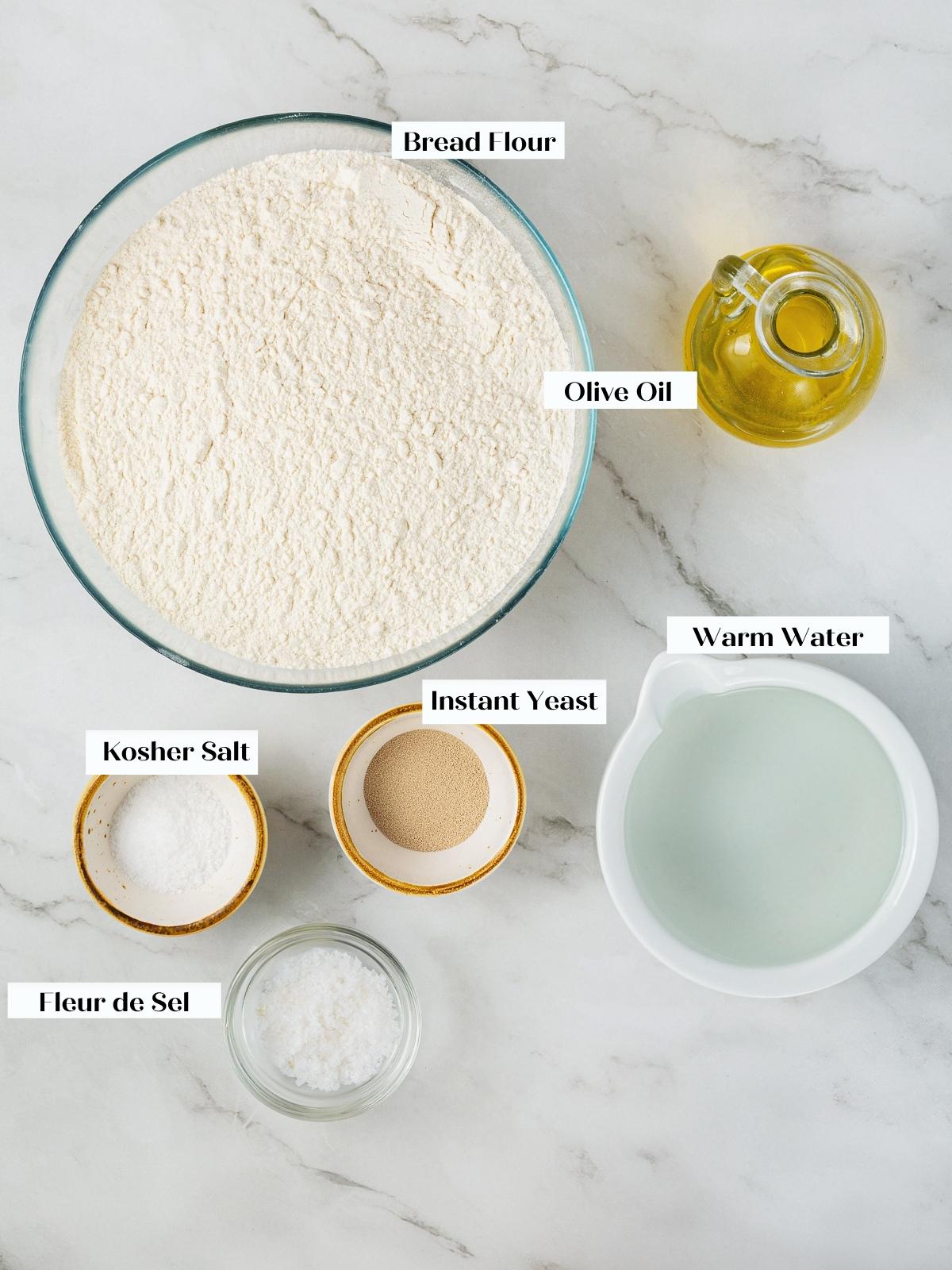 Ingredients for focaccia including flour, oil, water, and yeast spread out on the counter.