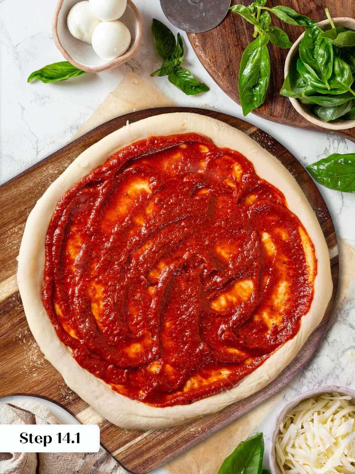 Pizza crust topped with sauce prepared from sourdough discard dough ready for toppings.