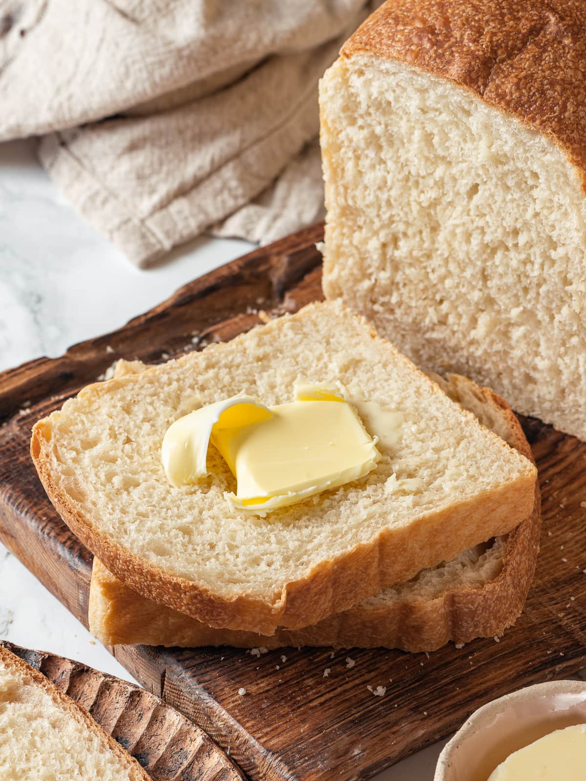 Small pad of butter on sliced sourdough bread, highlighting soft crumb and flavor.