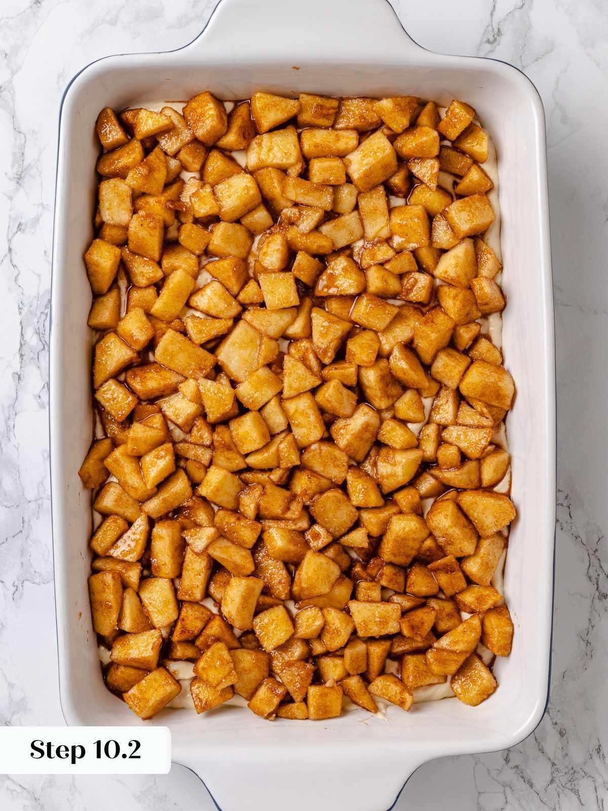 Baking pan showing apple mixture layered over first spread of cake batter.