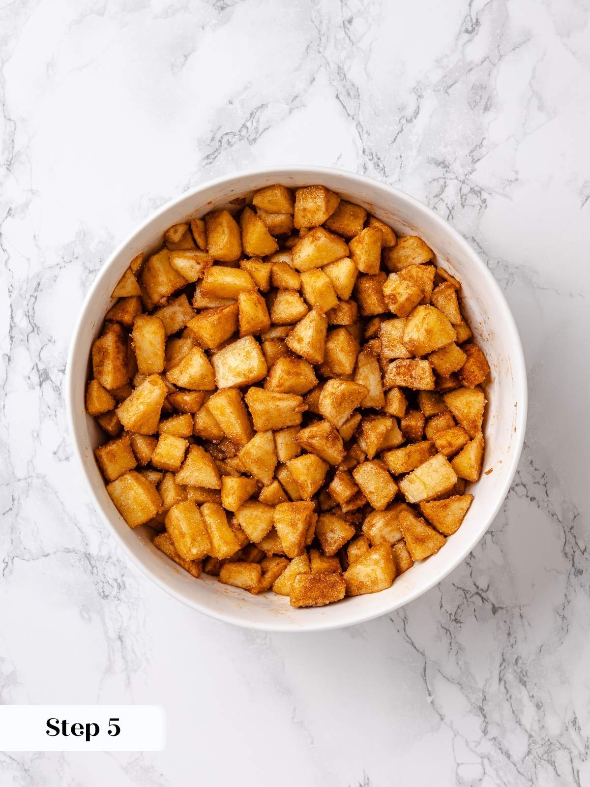 Bowl filled with diced apples coated in cinnamon sugar for coffee cake filling.