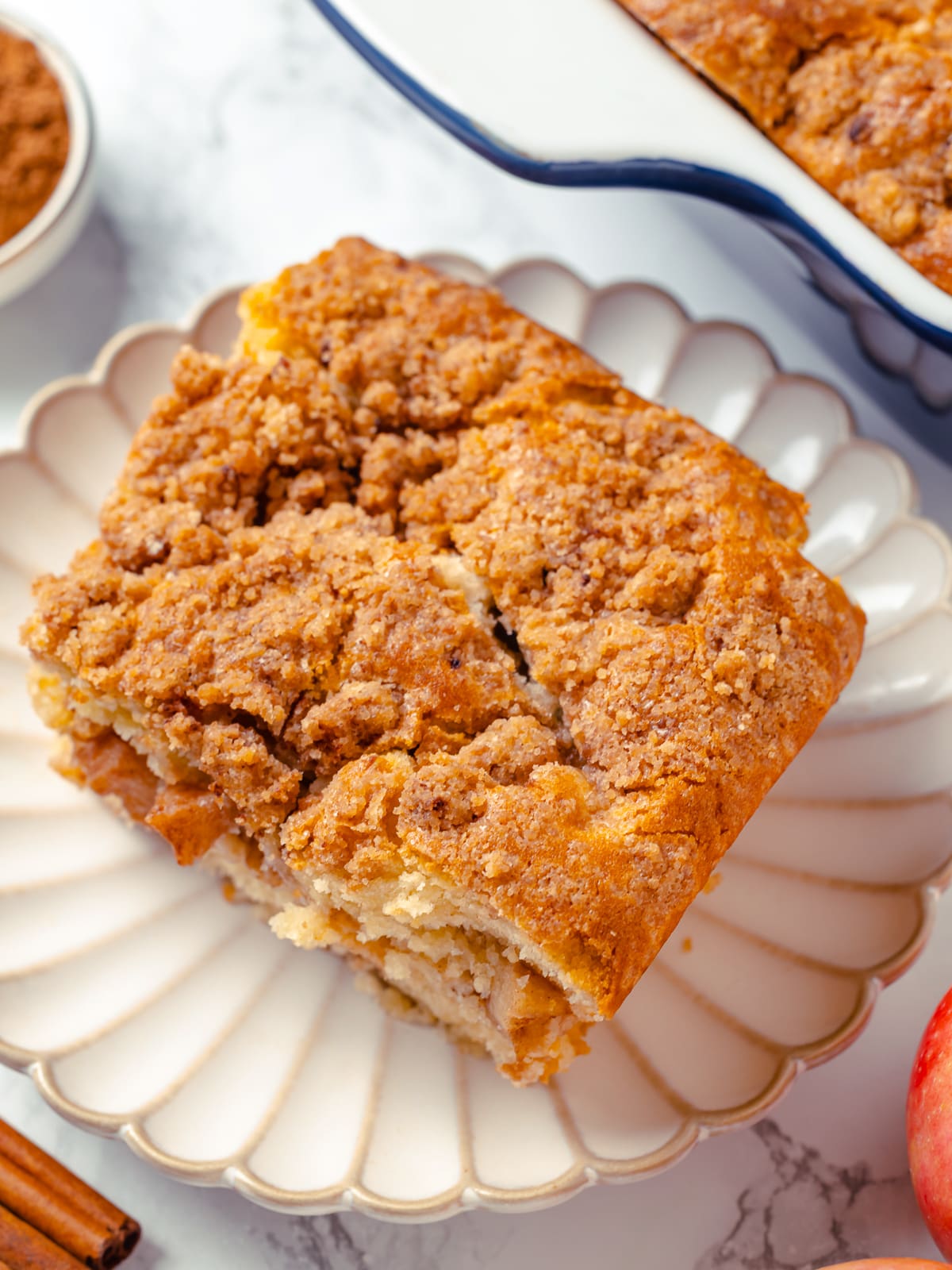 Slice of apple coffee cake served on a white scalloped plate with golden topping.