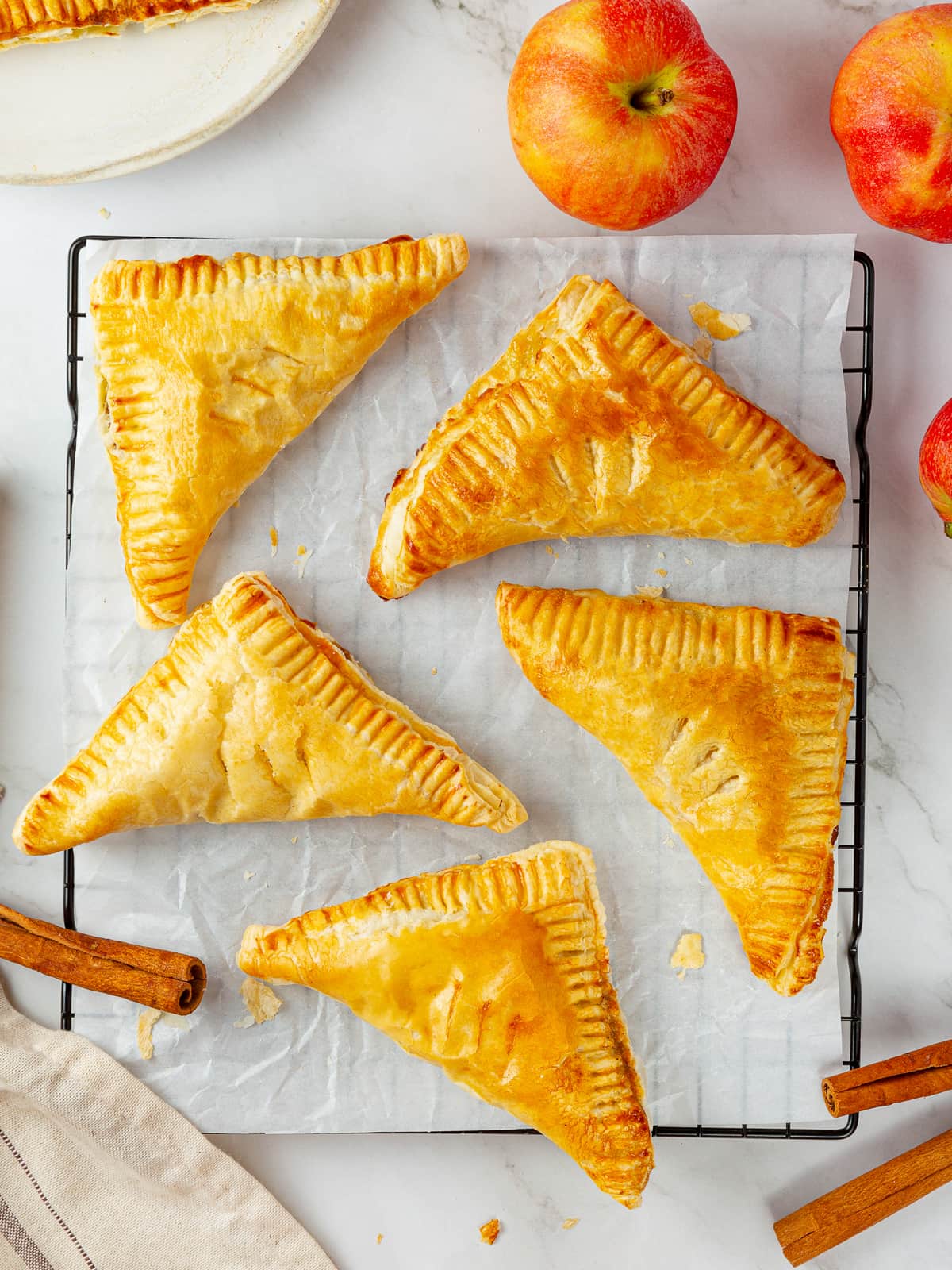 Apple turnovers cooling on parchment-lined tray, each golden and evenly baked.
