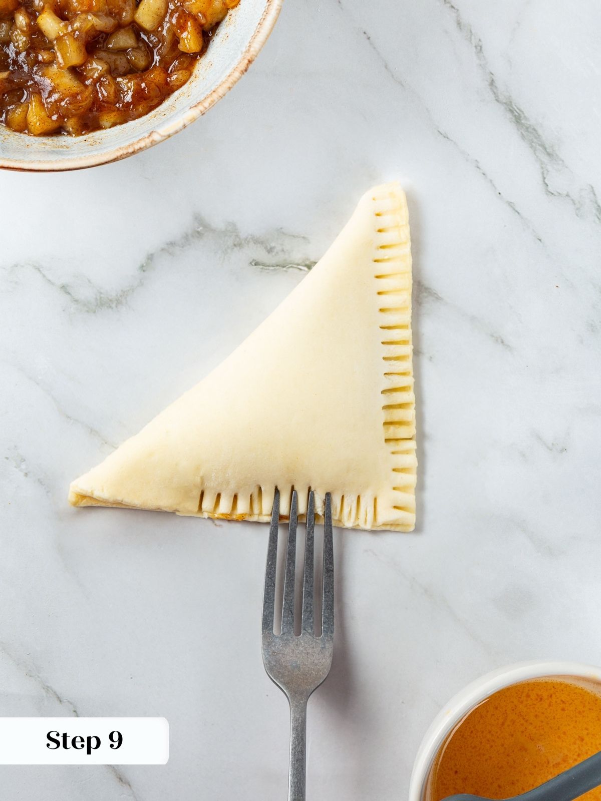Fork pressing edges of puff pastry turnover to create a secure crimped seal before baking.