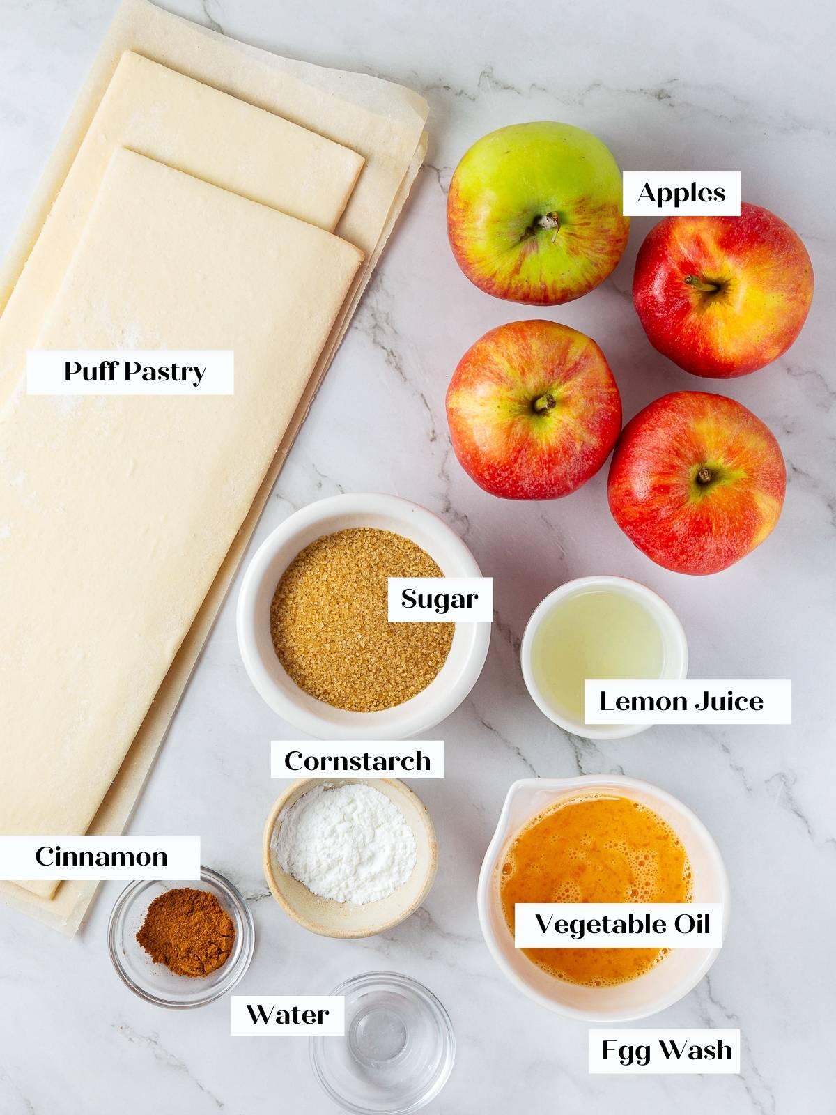 Puff pastry sheets, apples, cinnamon, and sugar arranged together on a countertop before baking turnovers.