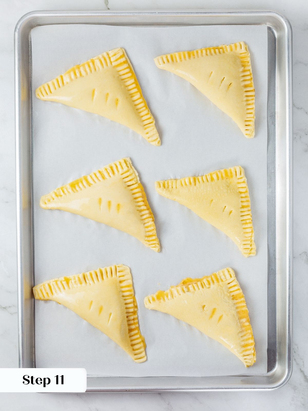 Unbaked puff pastry turnovers arranged neatly on parchment paper, filled and folded before baking.
