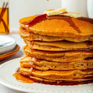 A pat of butter melting slowly over fluffy pumpkin pancakes, softening into golden layers.