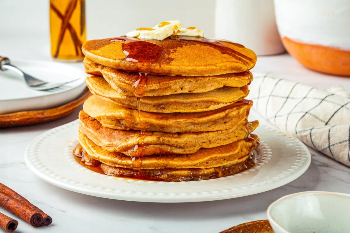 Pumpkin pancakes plated with cinnamon sticks beside them, emphasizing spiced fall breakfast flavors.