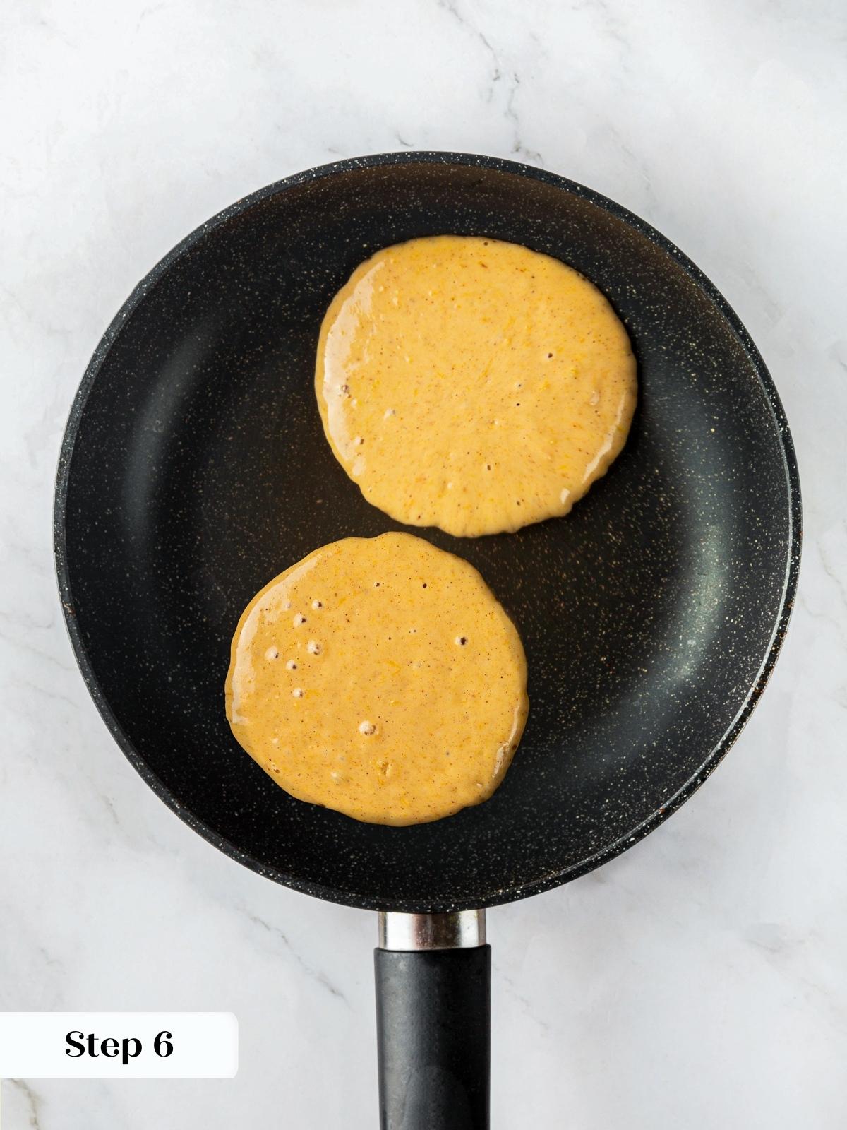 Pumpkin pancake batter cooking in a skillet, small bubbles forming as it turns golden brown.