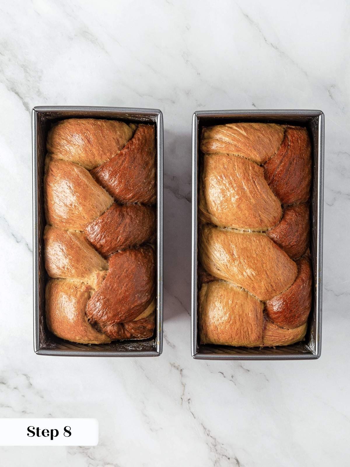 Fully baked marble rye loaves cooling in pans with golden crust and braided top.