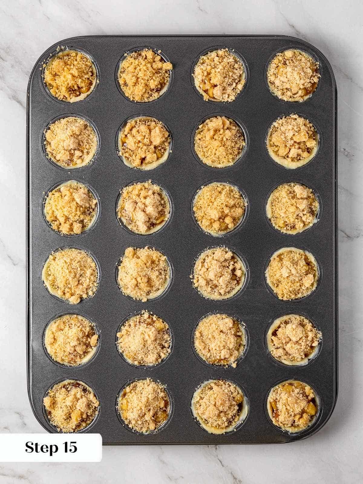 Crumble topping sprinkled over filled mini apple pies before baking in the oven.